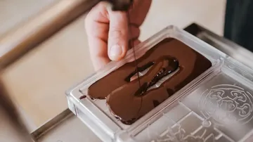 Hand, die flüssige Schokolade in eine Form gießt.