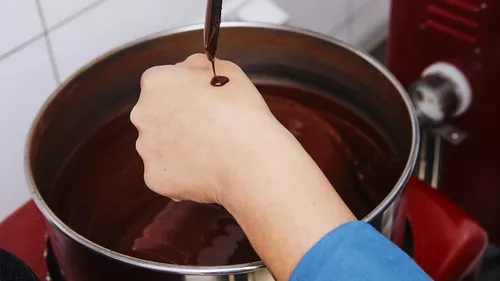 Hand tropft Schokolade aus einem Löffel in eine Schüssel.