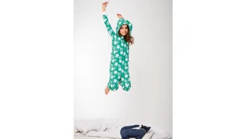 A girl jumps happily on a bed with blankets.