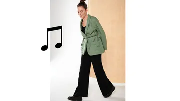 Woman in green blazer walks past a neutral background.
