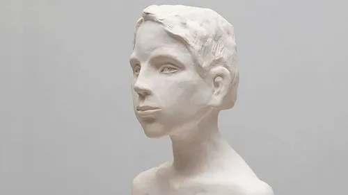 Skulptur eines Kopfes blickt nach vorne, neutraler Hintergrund.