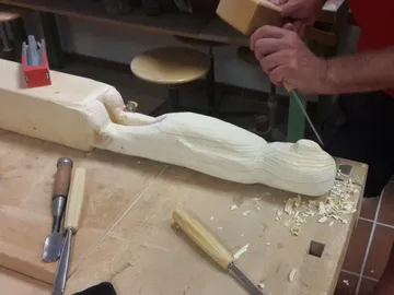 Wooden figure is worked with a tool in a workshop.