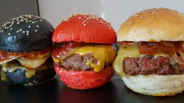 Drei bunte Burger mit Käse und Soße auf einem Tisch.