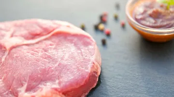 Rohes Fleischstück liegt neben einer Sauce auf Steinplatte.