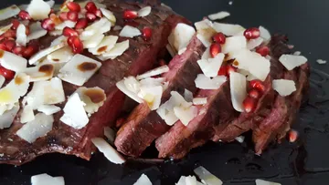 Sliced piece of meat, decorated with pomegranate and cheese.