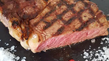 Grilled steak is on a black plate, with salt.