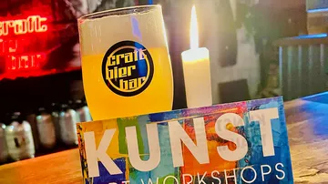 A glass of beer is placed next to a burning candle.