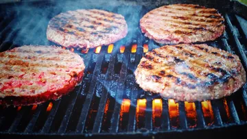 Grills fry hamburger patties over blazing flames.
