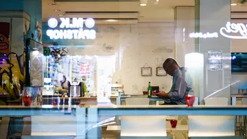 Mann sitzt alleine, tippt auf Handy, in modernem Café.