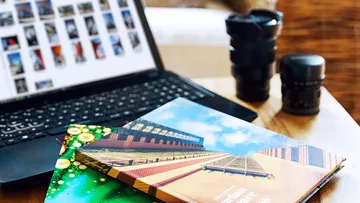 Laptop with photographic books and camera accessories on table.