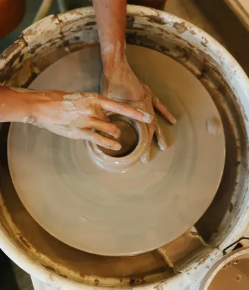 Hands form clay on a potter's wheel in a workshop.