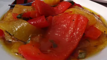 Bunte Paprika-Scheiben liegen in Öl auf einem Teller.