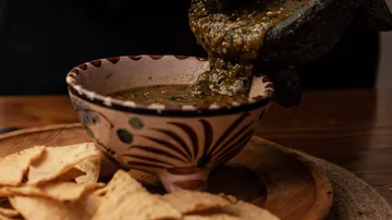 Salsa is poured into a decorative bowl over chips.