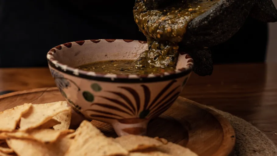 Salsa is poured into a decorative bowl over chips.