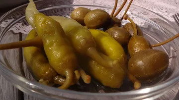 Yellow chilies and olives in a bowl on a table.