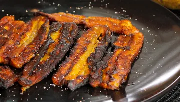 Roasted banana pieces on a black plate, lightly salted.