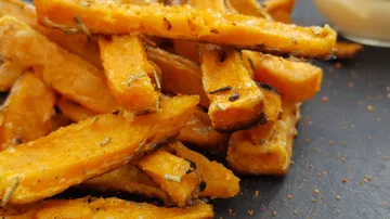 Süßkartoffel-Pommes liegen auf einem schwarzen Teller.