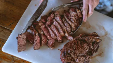 Sliced beef liegt auf einem Schneidebrett, Hände schneiden.
