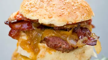 A burger with cheese, bacon and onions on a roll.