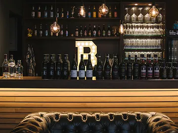 Bar mit Getränken, Beleuchtung und Holzregalen im Hintergrund.