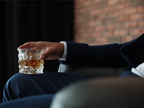 A man holds a whiskey glass in an elegant room.