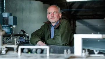 A man is standing relaxed at machines in a factory.