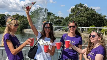Vier Frauen feiern am Wasser mit roten Bechern und Sekt.