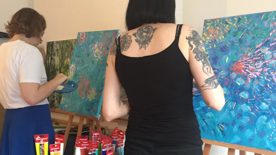 Zwei Künstlerinnen malen farbenfrohe Bilder in einem Studio.