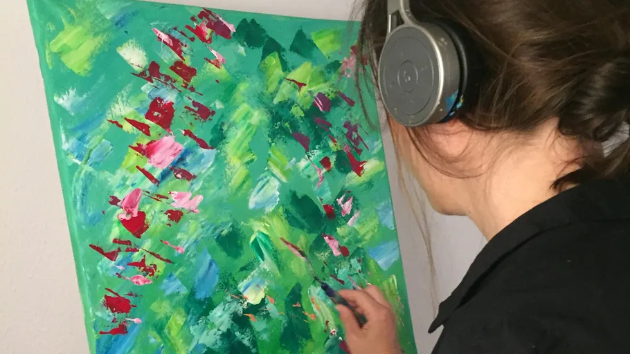 Person painting vibrant abstract canvas, wearing headphones.