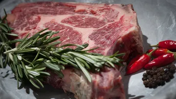 A piece of beef is covered with herbs and spices on paper.