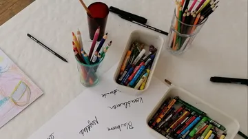 Farbstifte liegen auf einem Tisch, umgeben von Materialien.