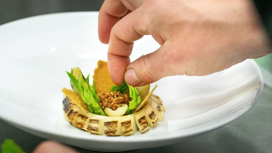 Hand adds ingredients to an artful, prepared dish.