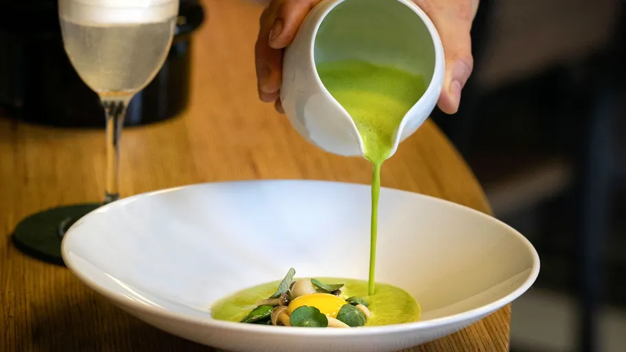 Green broth is poured into a white bowl.