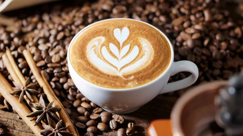 Tasse mit Kaffee, dekoriert, umgeben von Kaffeebohnen.