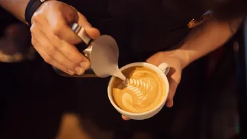 A hand pours milk into a latte style cup.