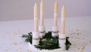 Four candles stand on a decorative plate with green.