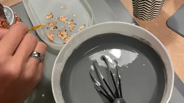 Hände mischen graue Farbe mit goldenen Stückchen in einer Schüssel.