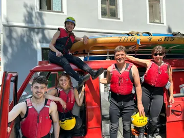 Five people in life jackets stand around a red car.