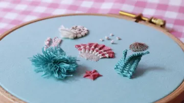Gestickte Muscheln und Pflanzen auf blauem Stoff, handwerklich.