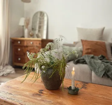 Blumentopf mit Pflanzen und brennender Kerze auf Tisch.