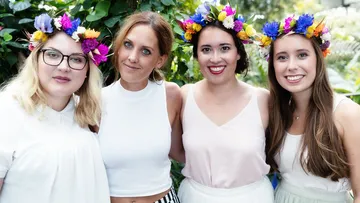 Four women wear flower wreaths and smile happily.