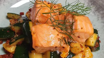 Lachsfilet ruht auf einem Gemüsebett mit Dill.