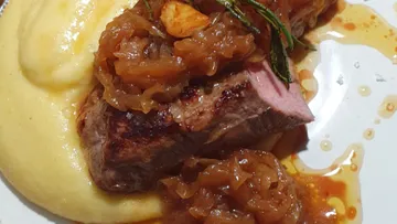 Saftiges Fleischstück mit Zwiebelsoße auf cremigem Püree.