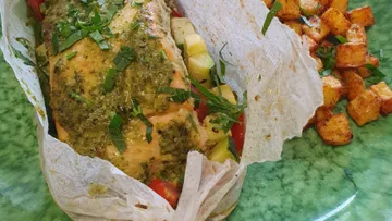 Salmon fillet with herbs surrounded by vegetables and potatoes.