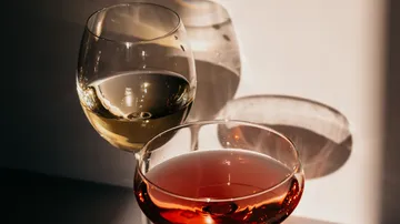 Two wine glasses stand and cast shadows on the surface.