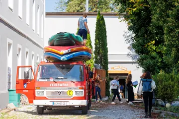 Feuerwehrwagen mit Booten, Mensch lädt sie auf. Sonniger Innenhof.