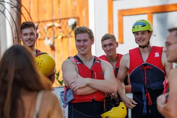 Five young men are wearing life jackets and laughing.