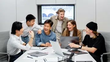 Sechs Personen lachen zusammen am Konferenztisch.