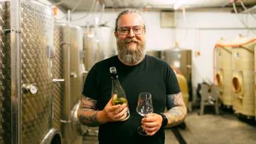 Bärtiger Mann hält Flasche und Glas in Weinkeller.