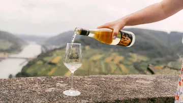 Eine Flasche gießt Wein in ein großes Glas, Blick ins Tal.